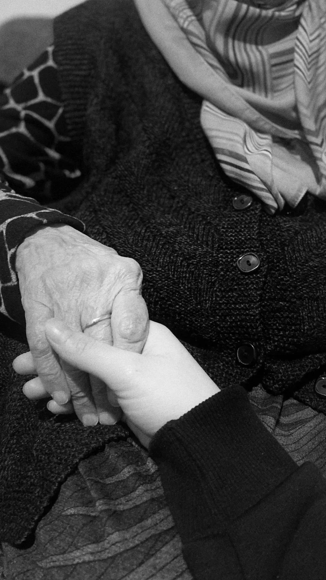 Une main âgée tenue avec douceur dans une autre main, en noir et blanc